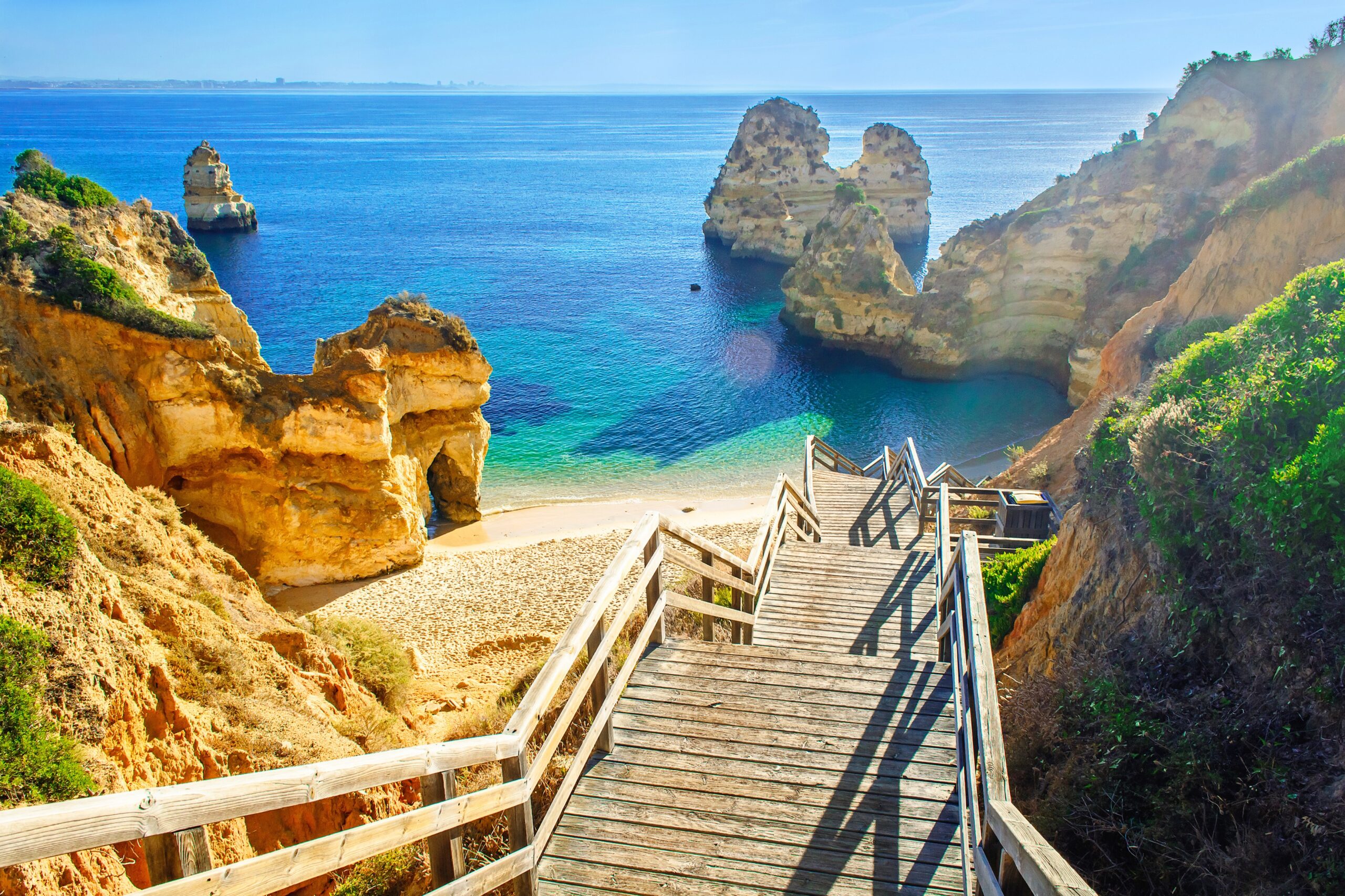 Wooden steps leading to Praia do Camilo beach near Lagos in Portugal with golden cliffs and turquoise Atlantic water