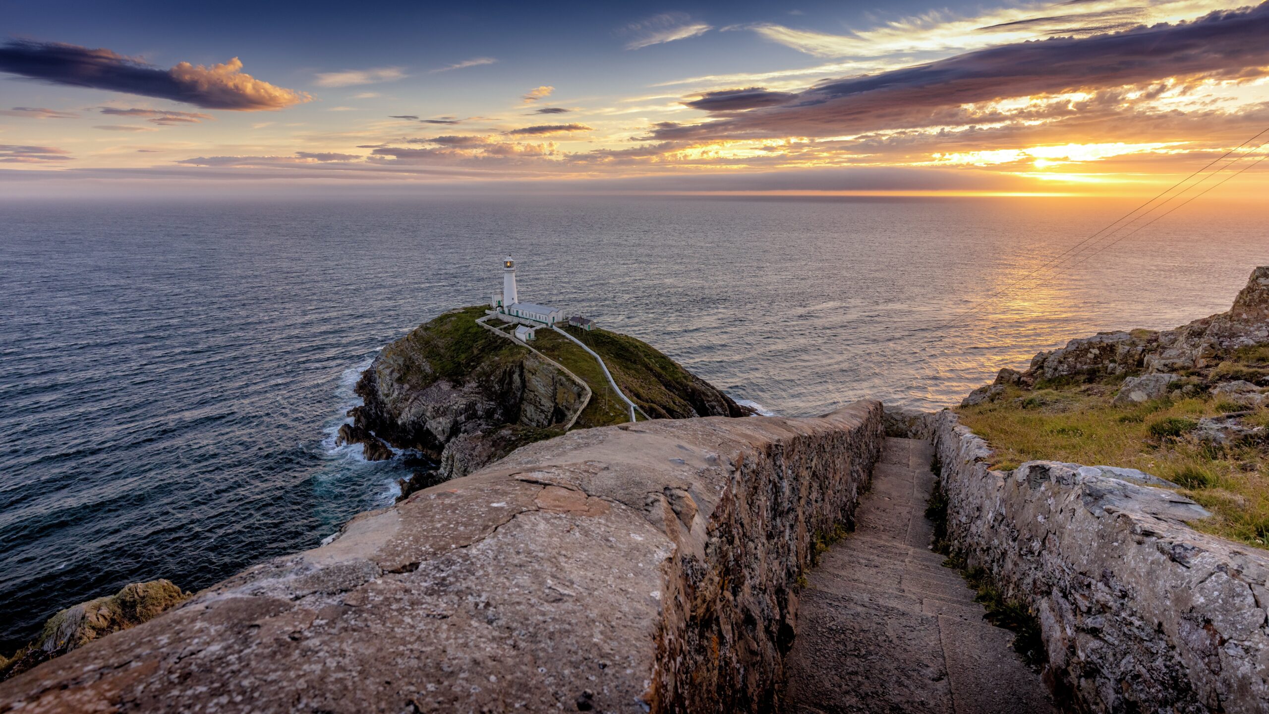 South Stack Lighthouse at sunset with stone coastal path steps showing managed access on Anglesey cliffs