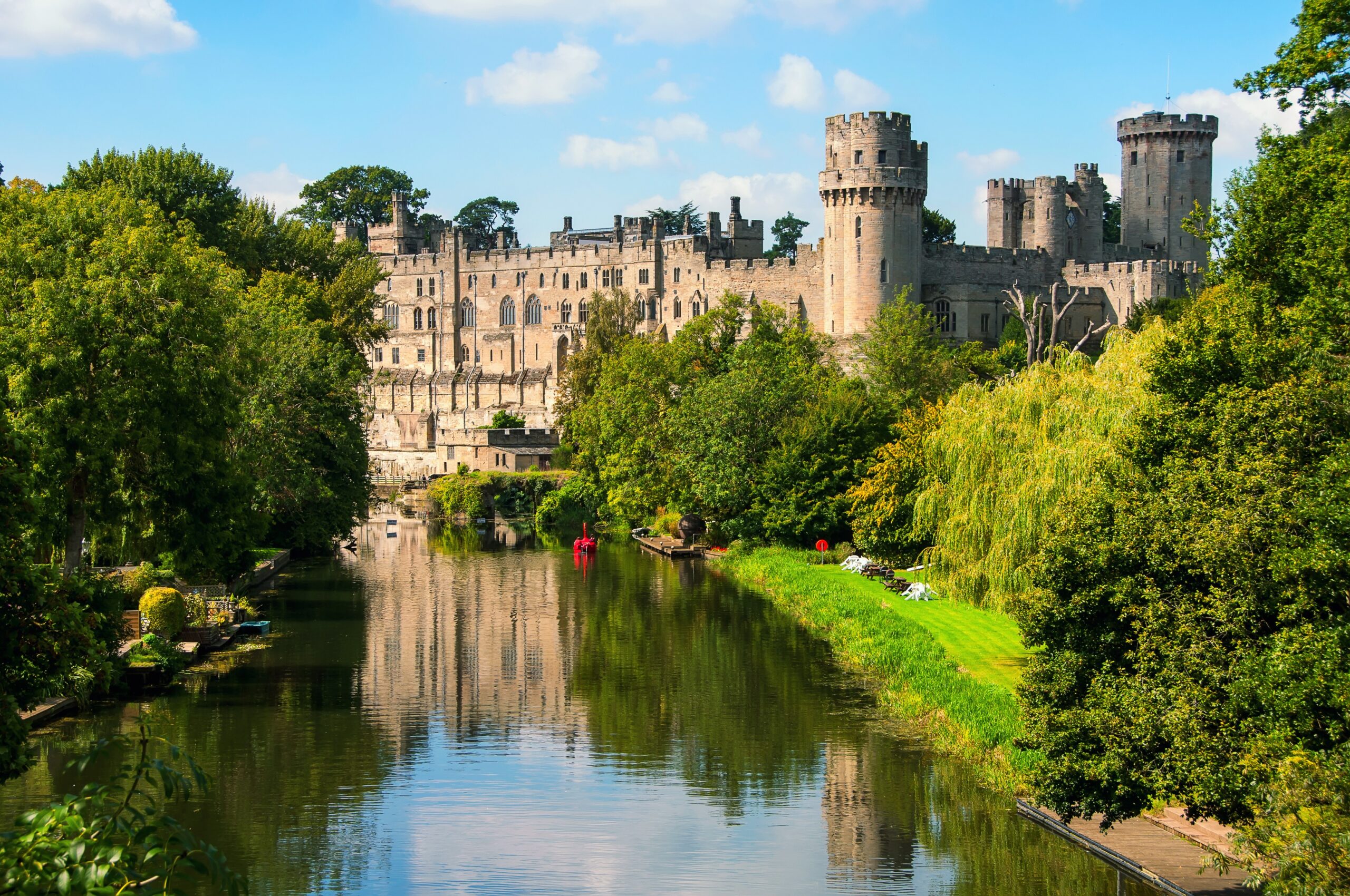 Warwick Castle viewed across the River Avon in summer with surrounding greenery in England