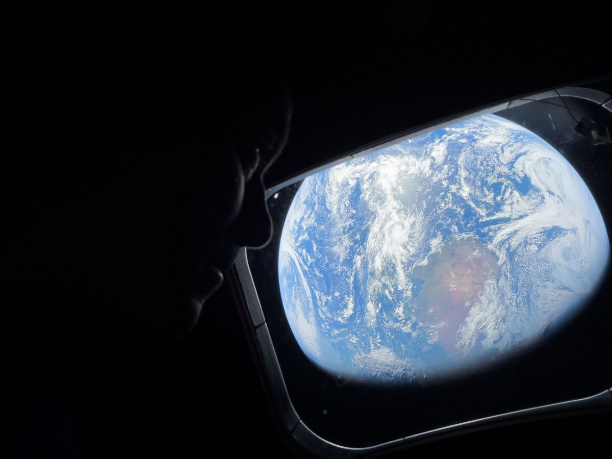Astronaut viewing Earth from space through spacecraft window during Artemis II mission