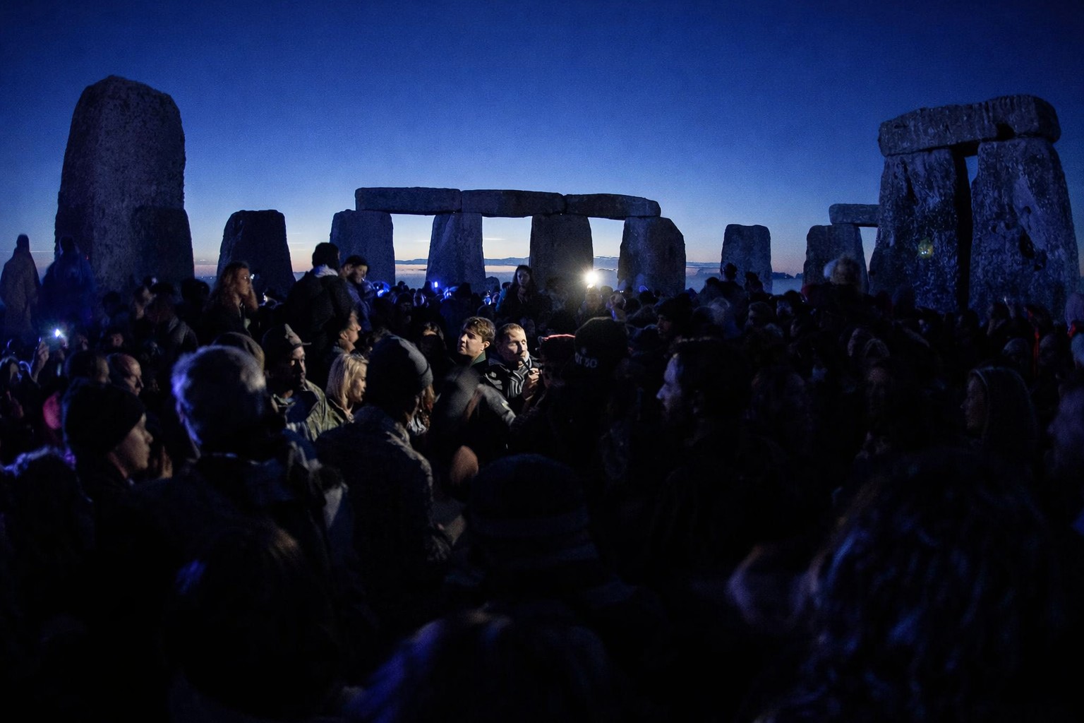Crowd gathered at Stonehenge before sunrise during the Summer Solstice event with early morning blue sky