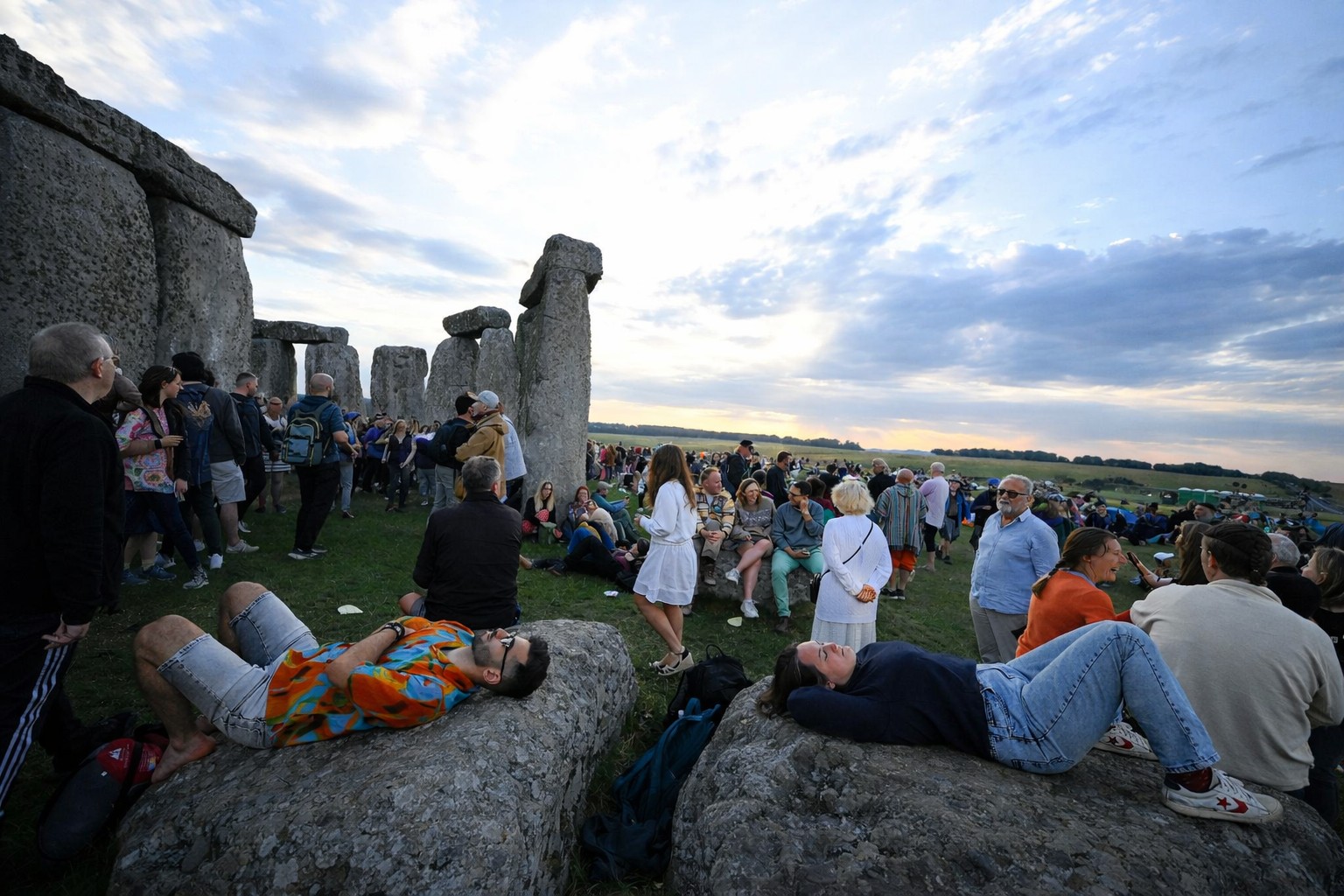 Stonehenge Summer Solstice visitors relaxing and gathering around the stones during the event in open landscape England